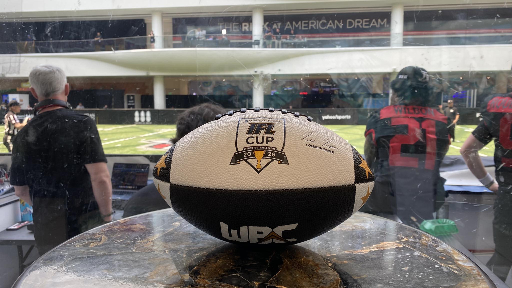 A photo of a game ball for the IFL Cup on a table, with a game going on in the background