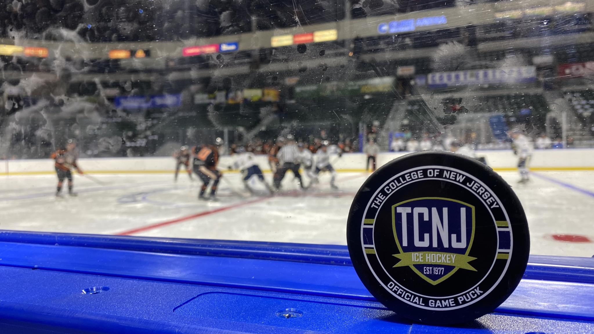 A photo of a hockey puck posed along the boards with a faceoff being taken in the background